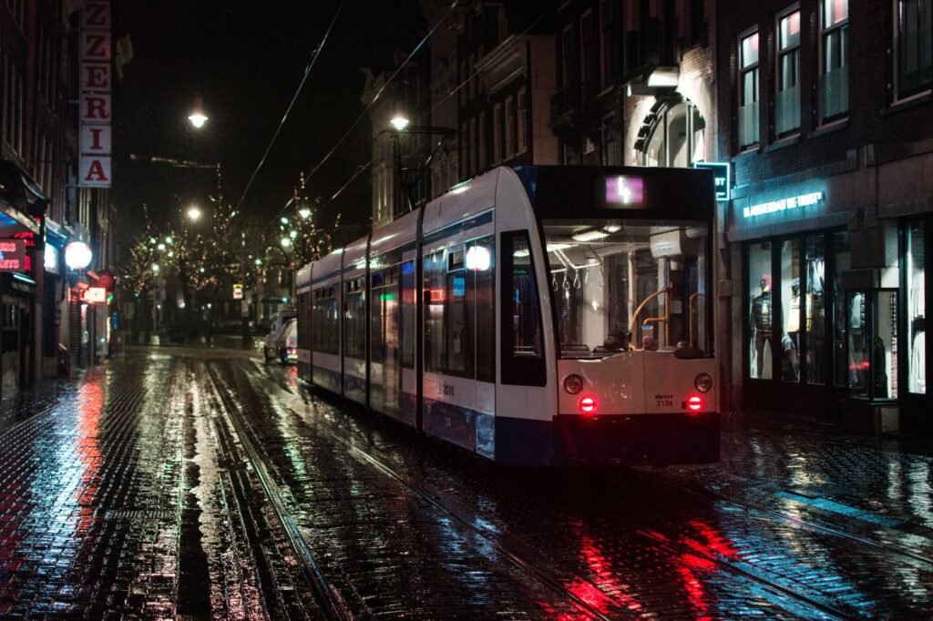 Een tram glijdt door de regenachtige straten van Amsterdam in de nacht, wat het openbaar vervoer benadrukt.
