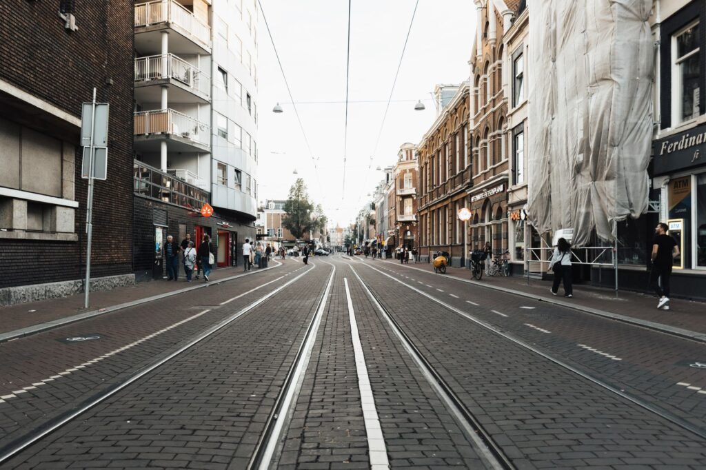 Straatbeeld van een stedelijke stad met tramrails, gebouwen en voorbijgangers in de schemering.