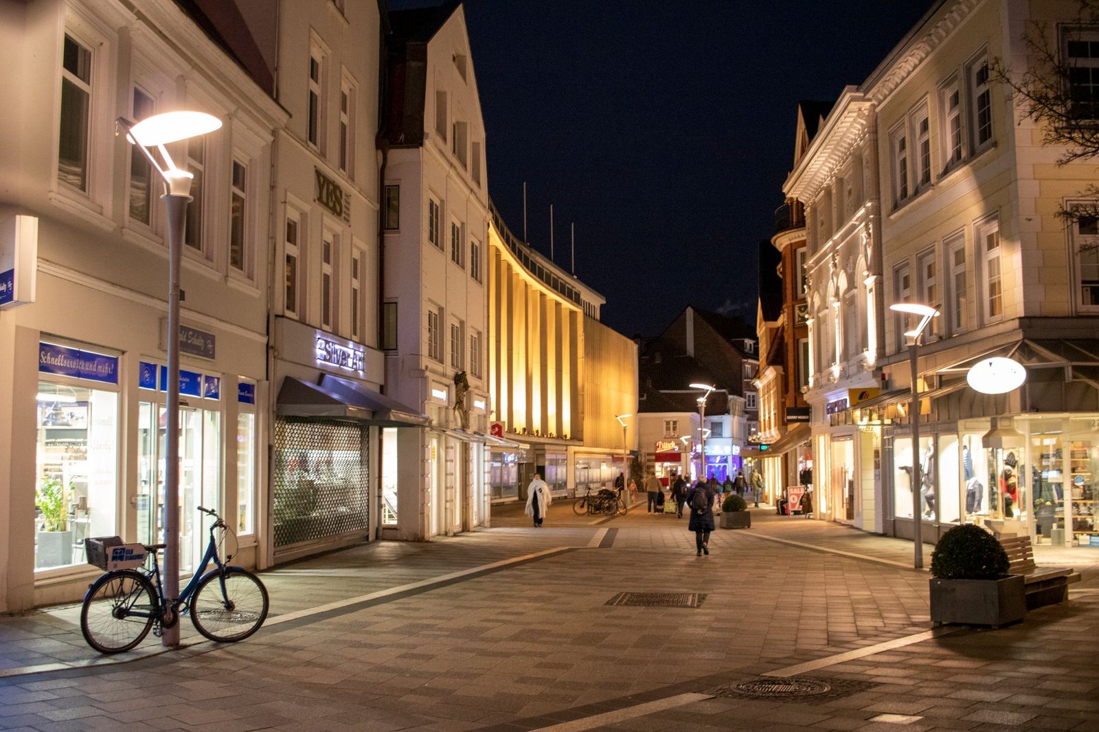 Nachtzicht op een levendige straat in Hamburg met verlichte gebouwen en rondslenterende mensen.