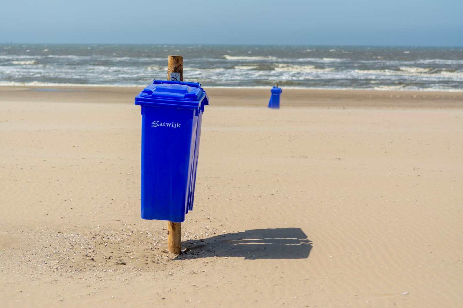 Zonovergoten strand met blauwe afvalcontainers aan zee in Katwijk aan Zee, Nederland.