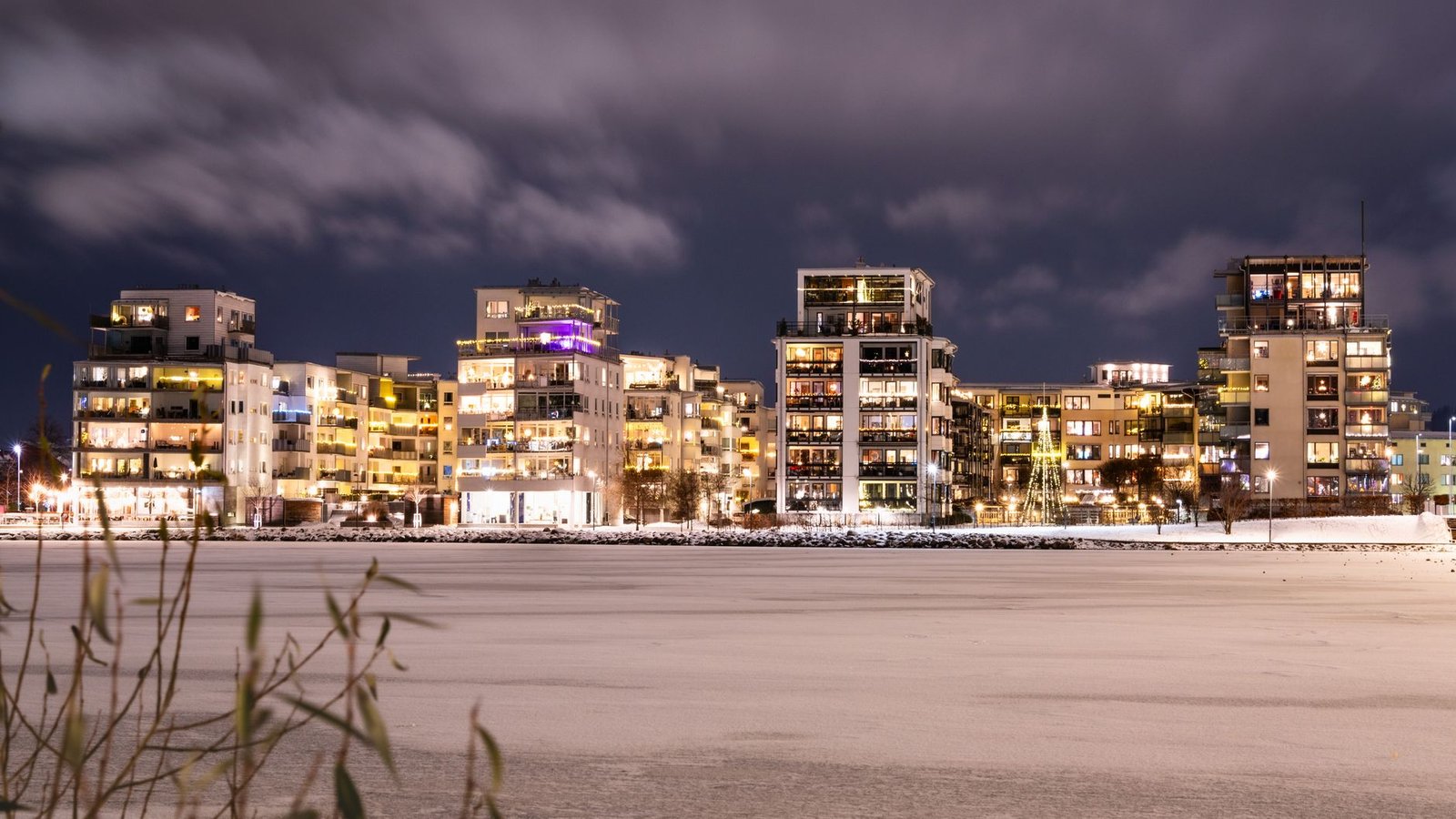 Een serene winteravond met verlichte gebouwen langs een bevroren rivier.